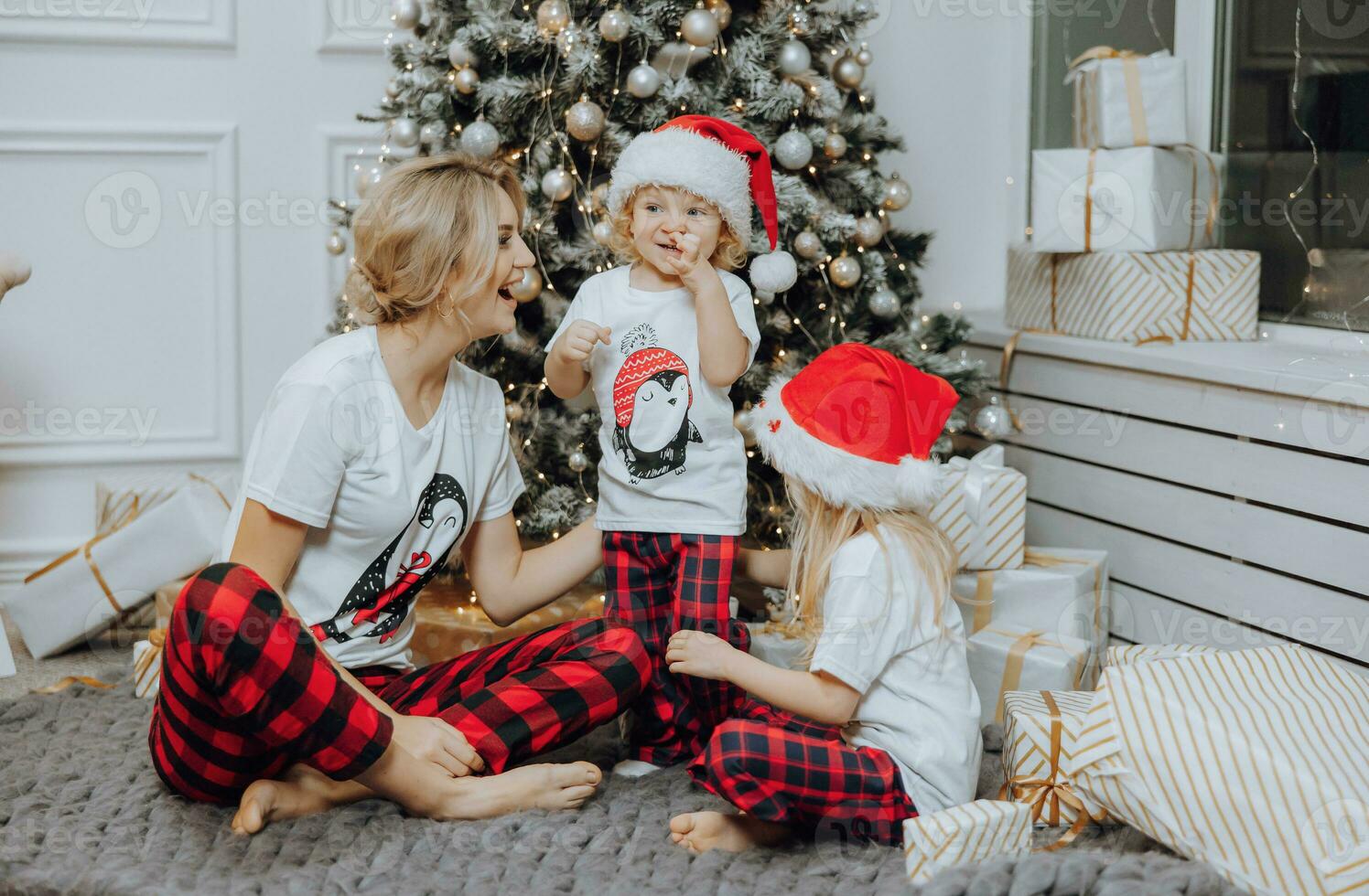 Cheerful and happy family with Christmas gifts near the Christmas tree in matching pajamas. Children are having fun. Loving family with gifts in the room. photo