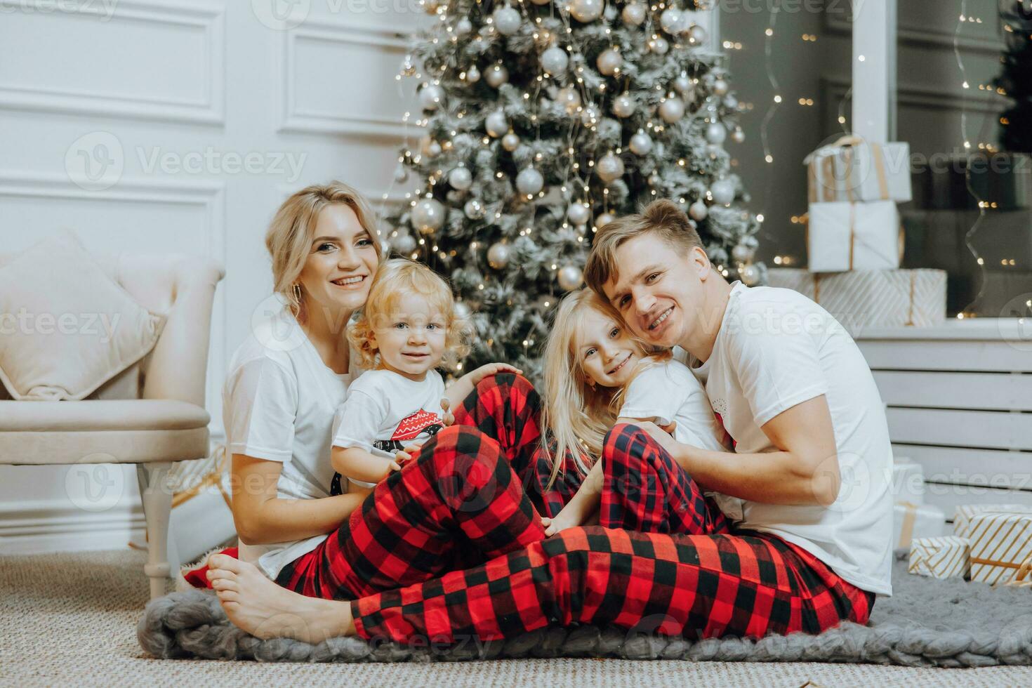 Cheerful and happy family with Christmas gifts near the Christmas tree in matching pajamas. Children are having fun. Loving family with gifts in the room. photo