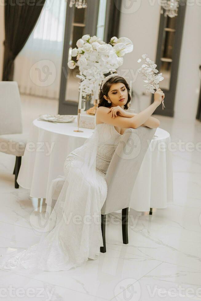 retrato de un hermosa niña en un Boda vestido. el novia en un lujoso vestido, sentado en un silla. vertical foto