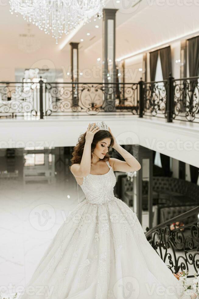 A beautiful bride in a white dress and a crown on her head in a chic interior photo