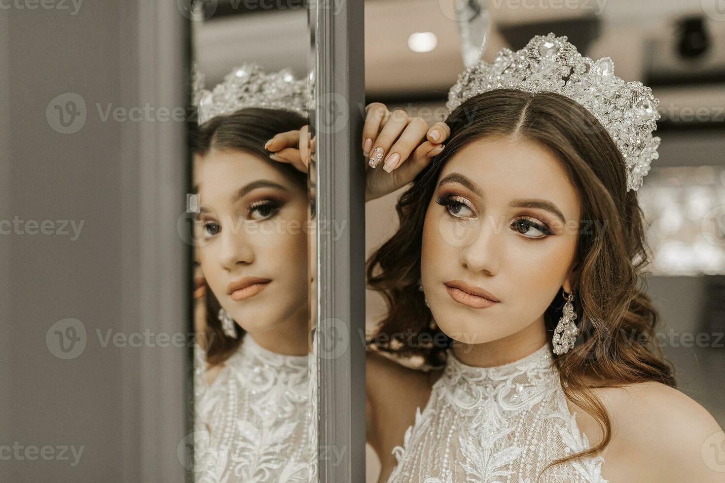 Portrait of a girl in a wedding dress near a mirror, with a crown on her head. The concept of a royal feast. Horizontal photo. photo