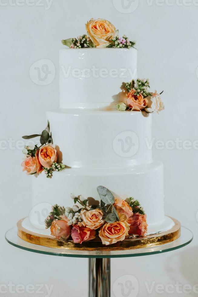 White three-tiered wedding cake decorated with orange roses. Festive dessert table with sweets. Wedding candy bar, various cakes, chocolate on stands. photo