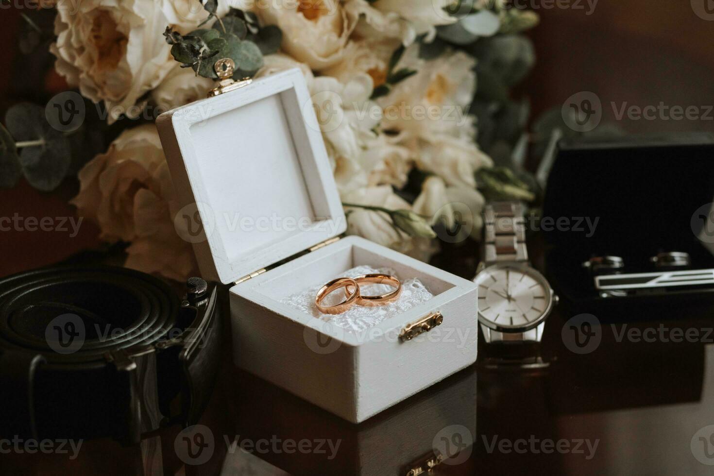 Wedding details on a brown background. Men's watch, cufflinks and black belt. Wedding bouquet, wedding rings in a white box decorated with flowers. photo