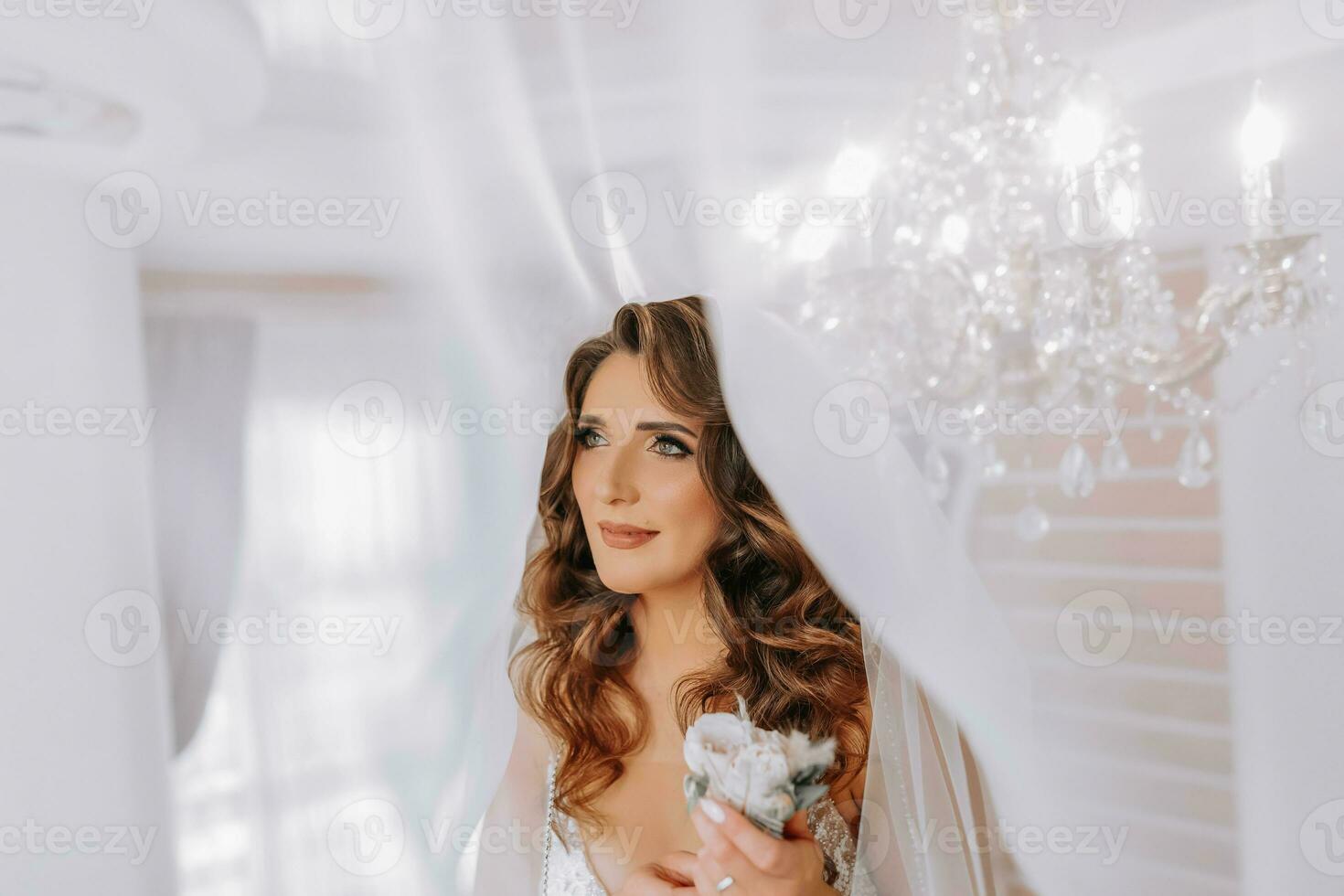 A beautiful bride in a wedding dress, holding rose boutonnieres under a veil photo