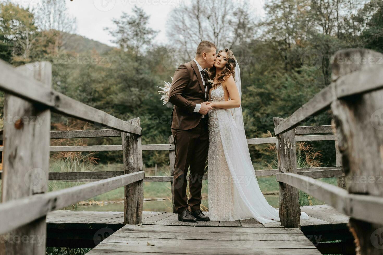 A young couple is kissing on the pier between the wooden fence on the background of the forest photo