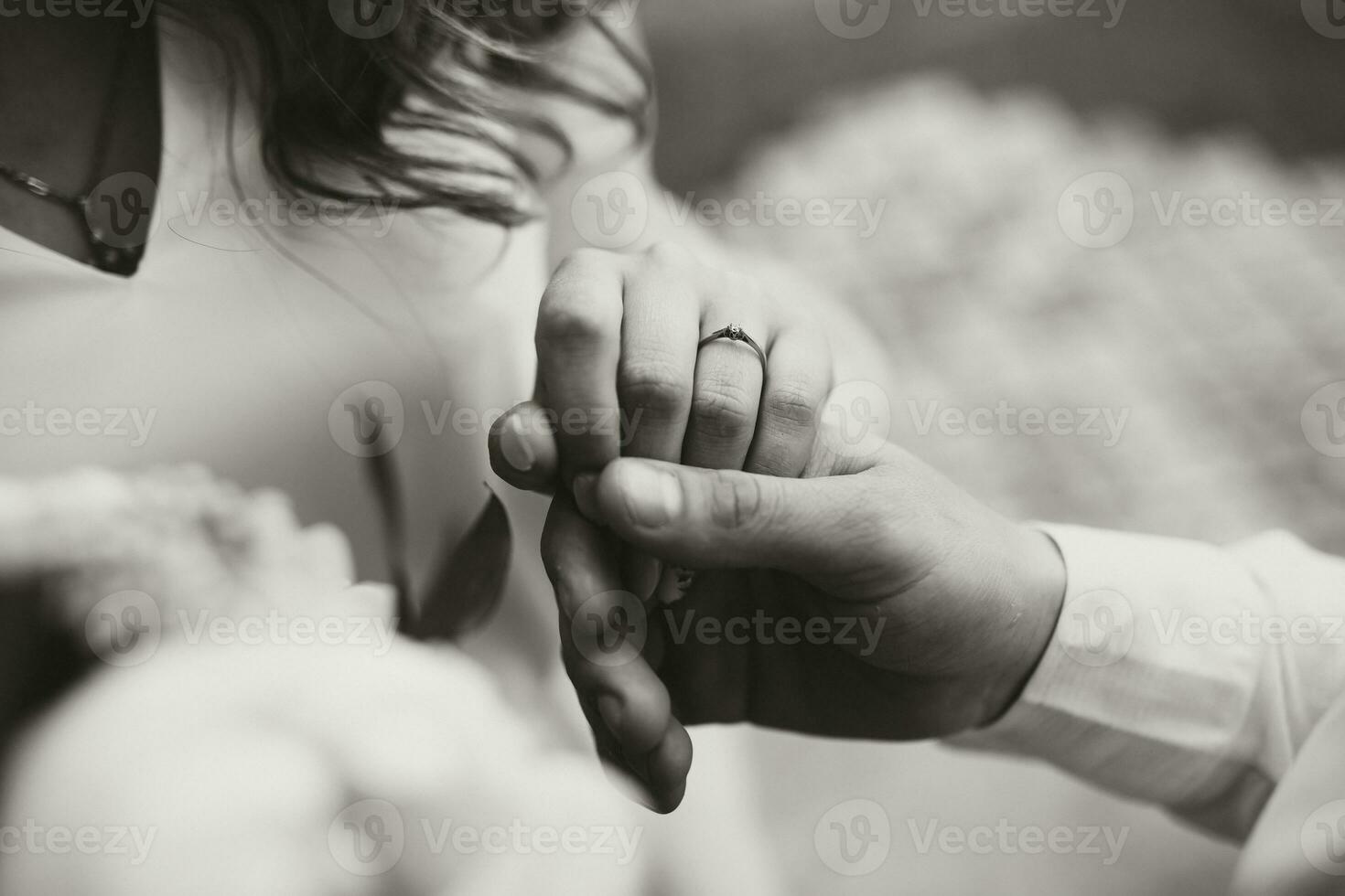 el novio sostiene el de la novia mano. joven Pareja en naturaleza. un hermosa Boda anillo en el dedo de el virgen. negro y blanco foto