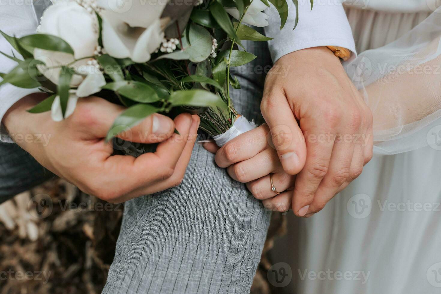 The bride and groom gently hold hands. They hold a bouquet in their hands. Close-up photo