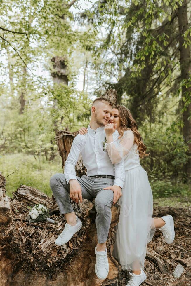 amable abrazo de el novia y novio en el bosque. el novio es vestido en un blanco camisa y gris pantalones, el novia es en un ligero blanco vestir foto