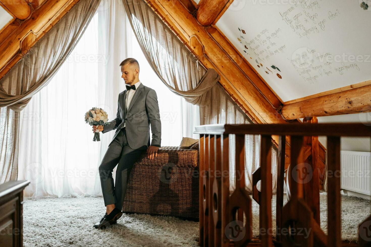 A young groom in a hotel room wearing a classic gray suit, white shirt and bow tie. Rest in wonderful apartments. The groom's morning at the hotel. Male hands close up photo