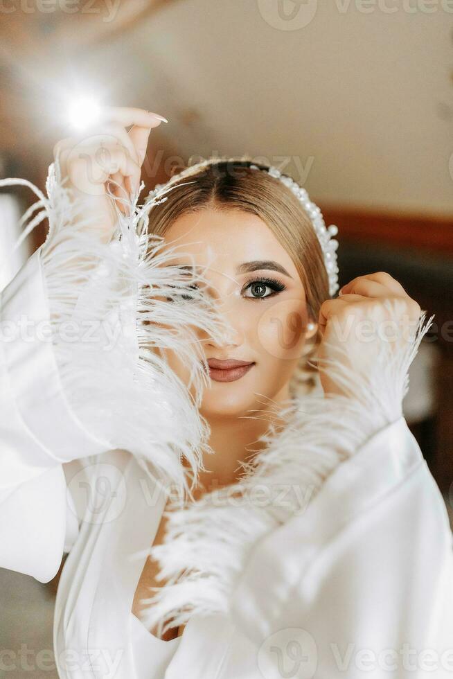 retrato de un hermosa novia en un hotel en un elegante blanco túnica con amplio mangas preparación para el Boda ceremonia. foto