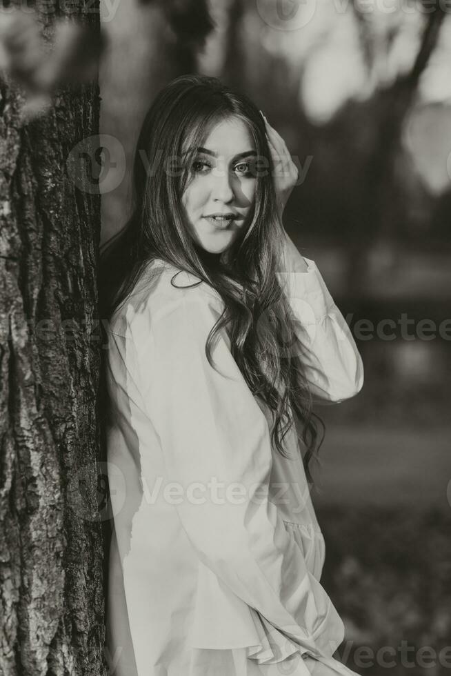 A pregnant woman in a white dress on a dark background poses in the park. Happy and carefree pregnancy. Autumn park. Happy woman enjoying her pregnancy. Black and white photo