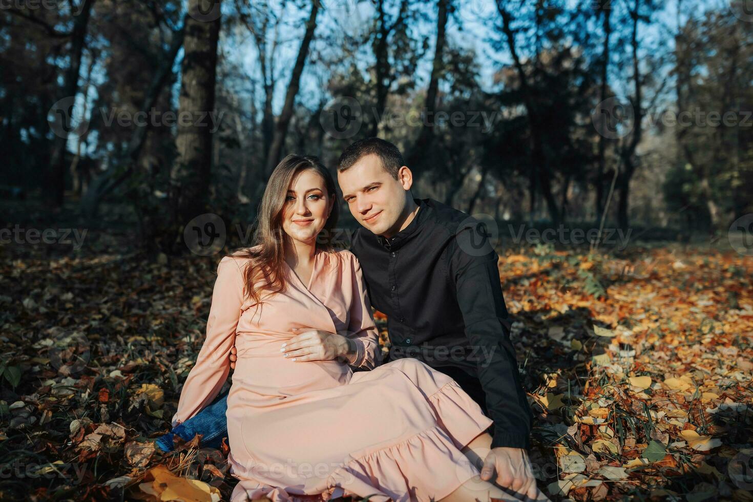 A man touched his pregnant wife's belly with his hand while resting in an autumn forest on a yellowed leaf. Support of the husband during pregnancy photo