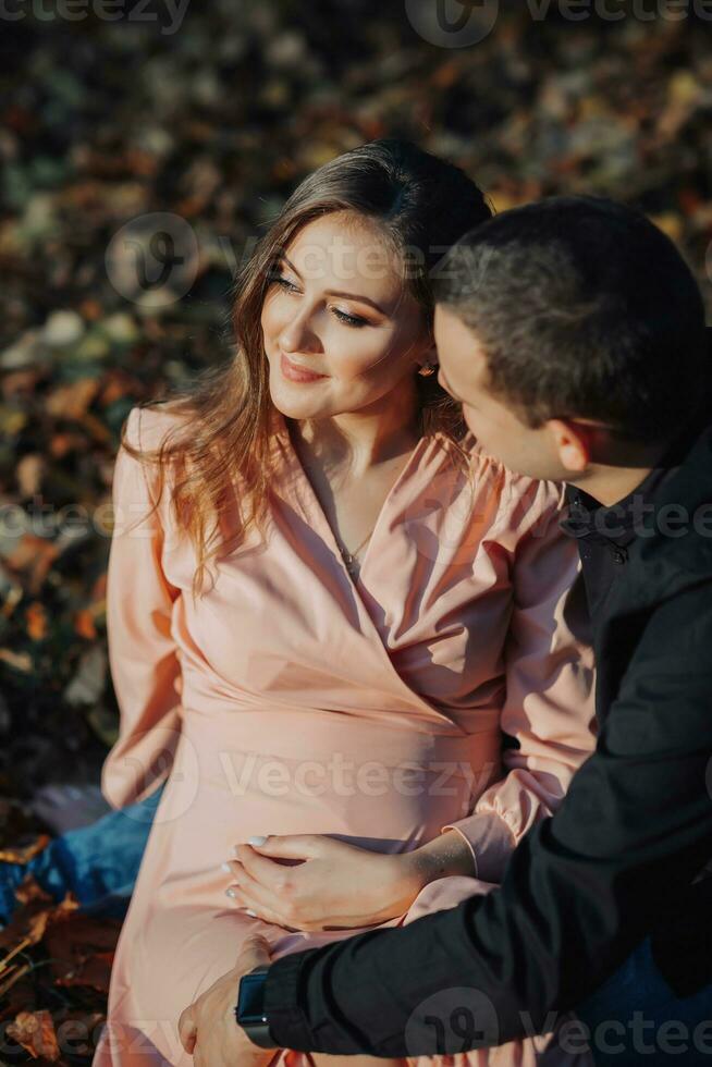 A man touched his pregnant wife's belly with his hand while resting in an autumn forest on a yellowed leaf. Support of the husband during pregnancy photo