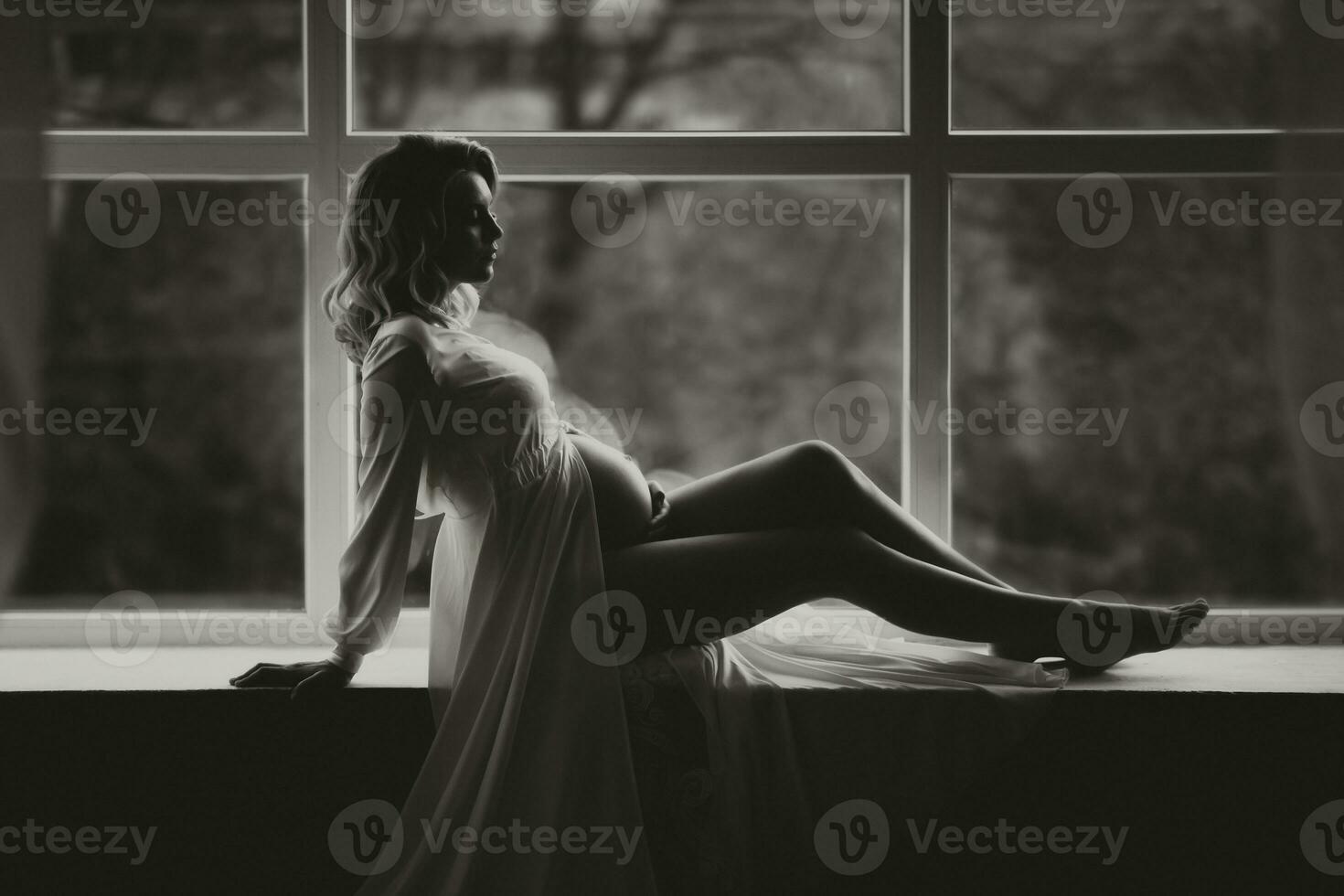 studio portrait, close-up, of a beautiful pregnant young woman on a white bed, holding her pregnant belly with her hands photo