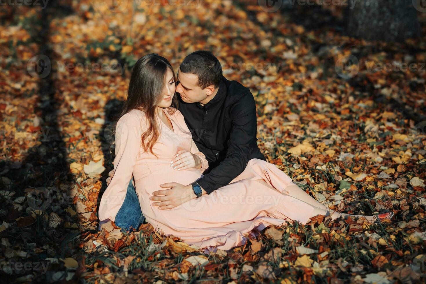 A man touched his pregnant wife's belly with his hand while resting in an autumn forest on a yellowed leaf. Support of the husband during pregnancy photo