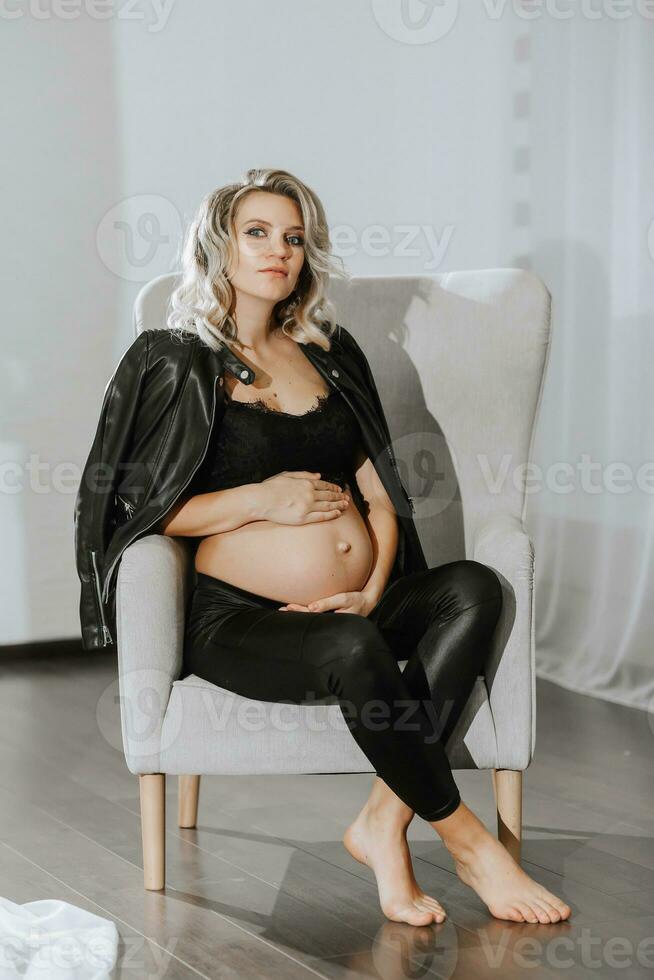 elegante estudio retrato de un hermosa embarazada joven mujer en un silla en un negro traje foto