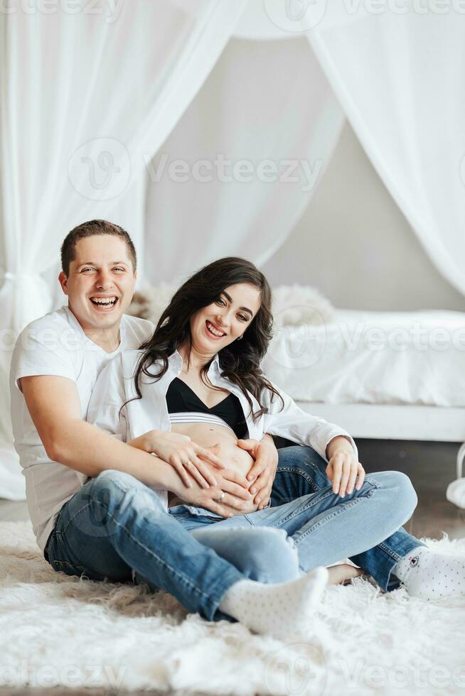 modern beautiful pregnant woman in jeans and shirt with her husband at home, caring, hugging, kissing. Concept of pregnancy, motherhood, preparation and waiting. The beauty of a woman during pregnancy photo