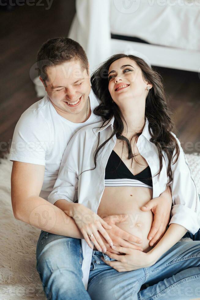 modern beautiful pregnant woman in jeans and shirt with her husband at home, caring, hugging, kissing. Concept of pregnancy, motherhood, preparation and waiting. The beauty of a woman during pregnancy photo