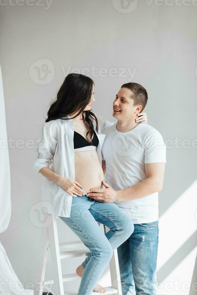 modern beautiful pregnant woman in jeans and shirt with man hugging her tummy with hands in beautiful sunlight. Concept of pregnancy, motherhood, preparation and waiting. photo