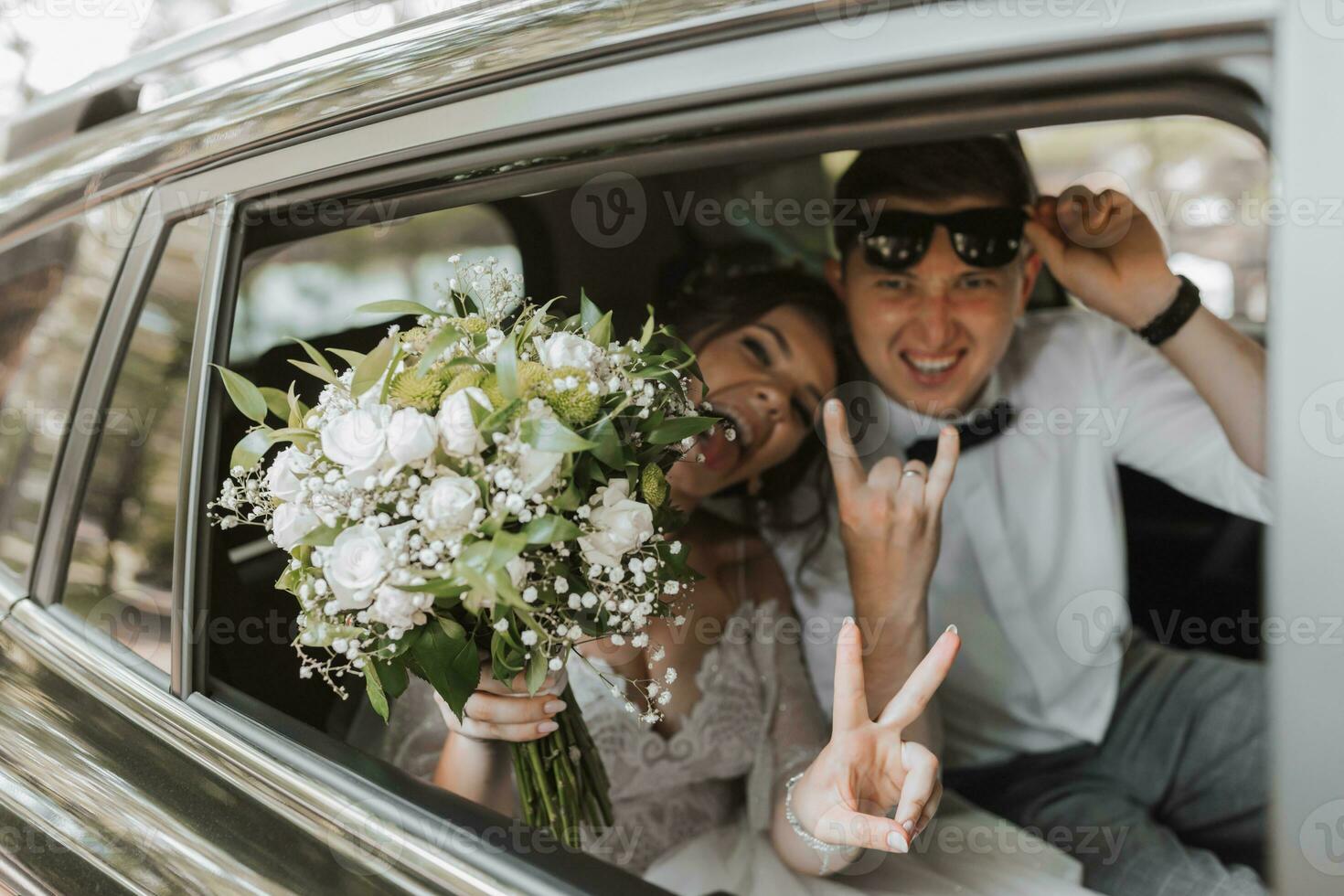 young happy bride and groom are rejoicing after the wedding ceremony in their car photo