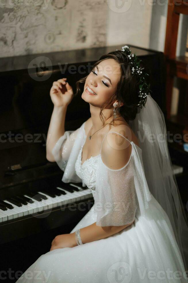 Portrait of a beautiful girl in a wedding dress and a wreath of fresh flowers on her head, playing the piano, playing alone photo
