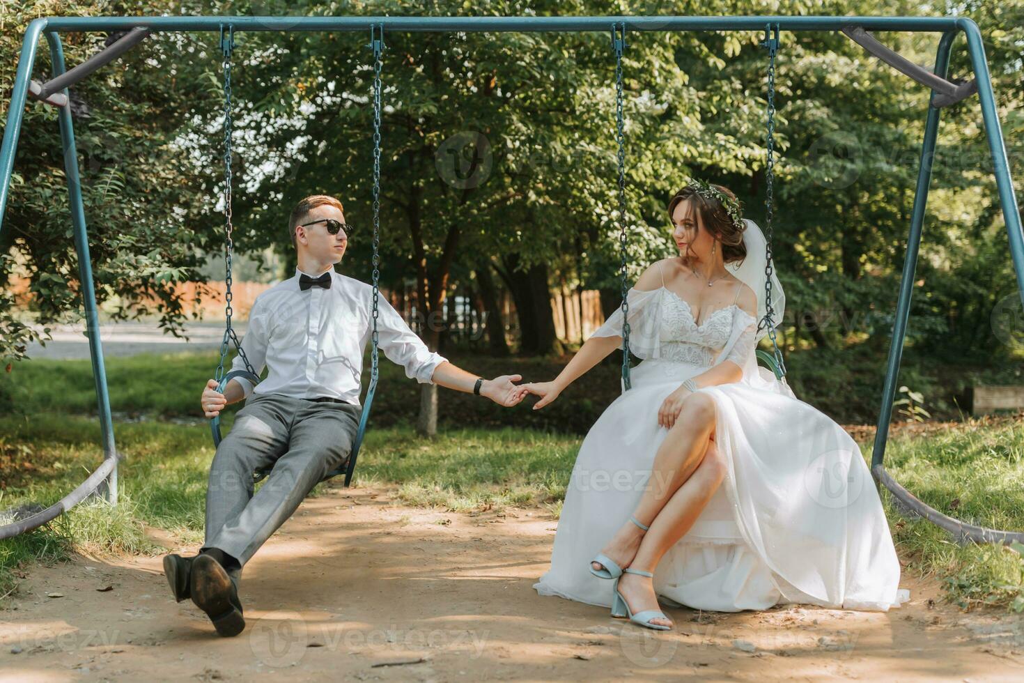 the bride and groom are sitting on a children's swing and holding hands photo