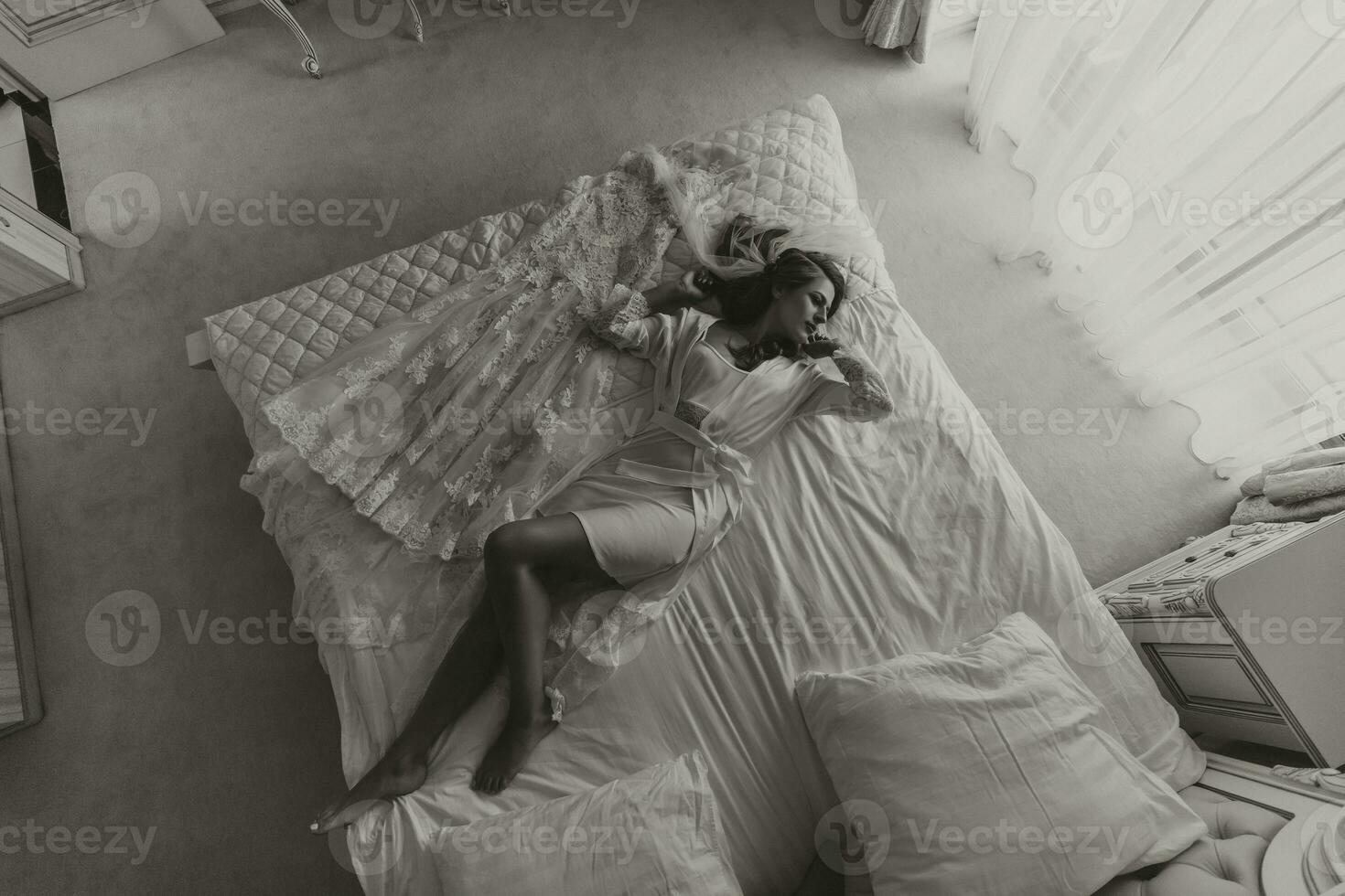 Beautiful young bride in a white peignoir lying on the bed in his bedroom. Last preparations for the wedding. The bride is waiting for the groom. Morning, the bride. photo