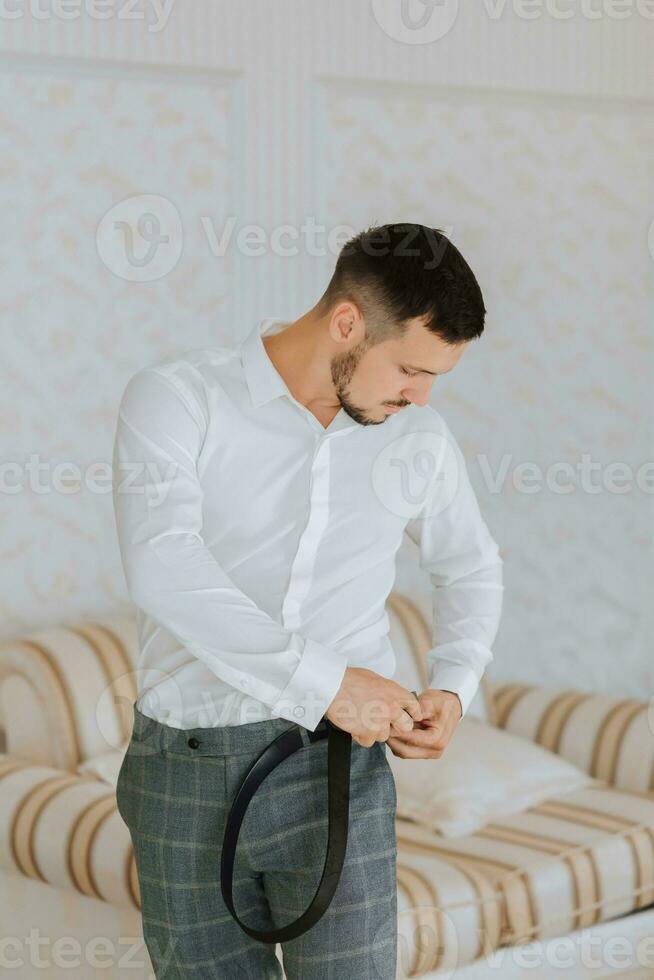 A stylish groom with a beard is preparing for the wedding ceremony. Groom's morning. Businessman wears a white shirt, the groom is getting ready in the morning before the wedding ceremony photo