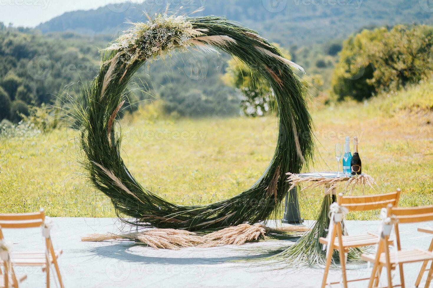 The wedding arch in the park is made of dry reeds on the background of the forest in blurred focus. Away wedding ceremony. Decorated chairs for the ceremony photo