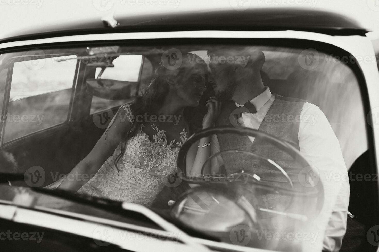 a luxurious and elegant wedding couple tenderly embrace in the middle of a stylish retro car. The photo was taken through the windshield. gorgeous bride and handsome groom in retro style.