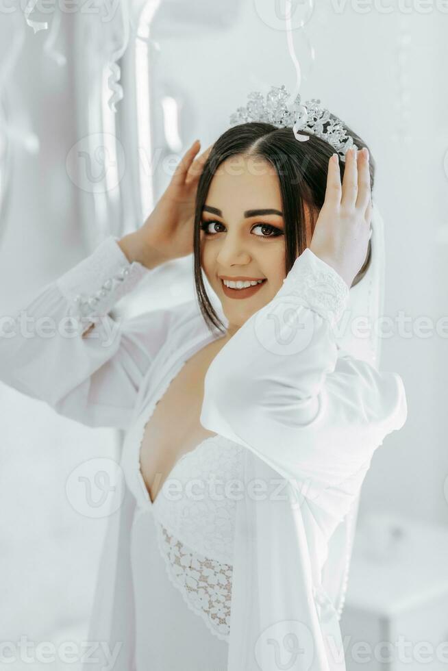 A beautiful bride girl in a white robe, veil and tiara on her head, the sun shines on her from the window. Happy young girl under the glare of sunlight. wedding concept photo