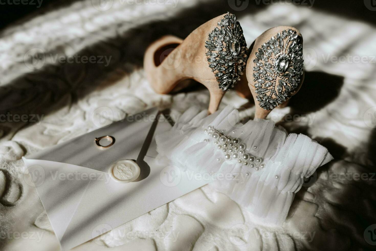 wedding shoes of the bride on a high heel of beige color with stones above the heel, an envelope with a wedding vow and a wedding ring of the bride is standing next to it photo