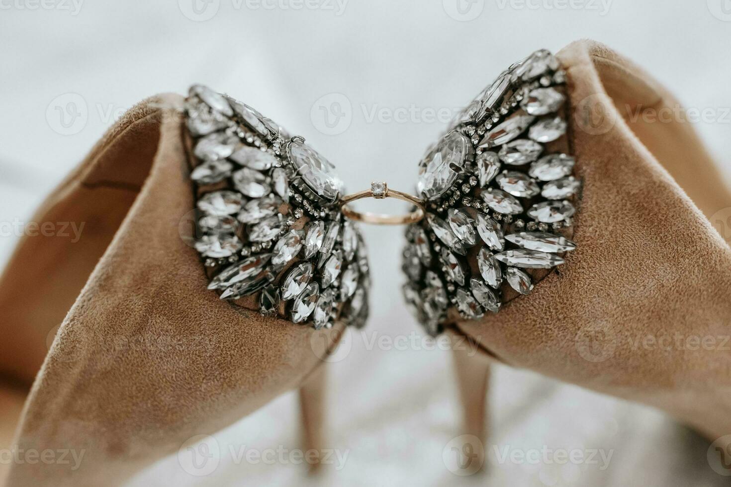 wedding shoes of the bride on a high heel of beige color with stones above the heel, between the shoes a gold ring of the bride photo