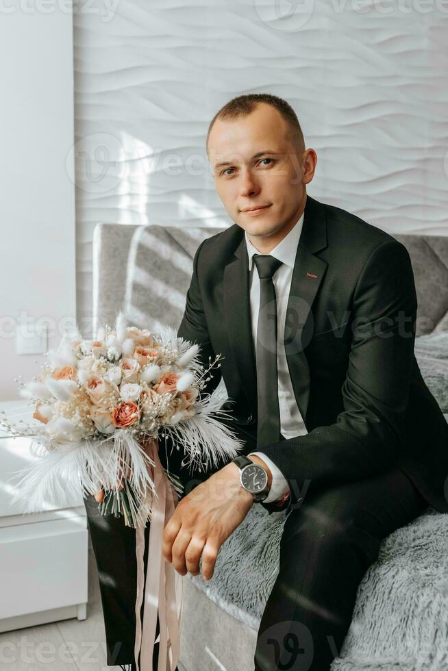 wedding bouquet of pink roses, feathers and dried flowers in the hands of the groom photo