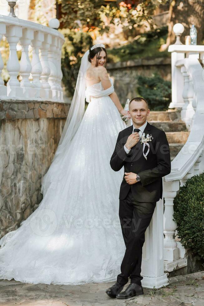 Full-length portrait of bride and groom on garden steps, groom in foreground photo