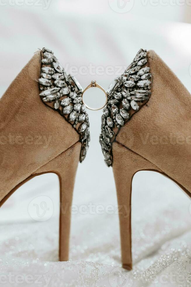 wedding shoes of the bride on a high heel of beige color with stones above the heel, between the shoes a gold ring of the bride photo