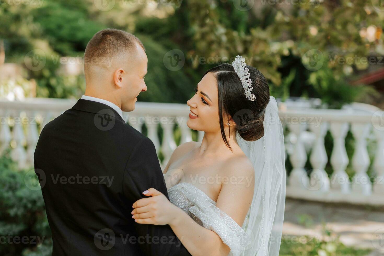 portrait of a young beautiful wedding couple in the garden, the bride in an off-the-shoulder wedding dress, the groom in a black classic suit photo