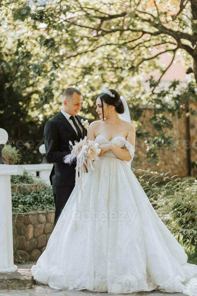 European wedding couple in the park. The bride in a beautiful dress with a long train and sleeves. Groom in a classic suit photo