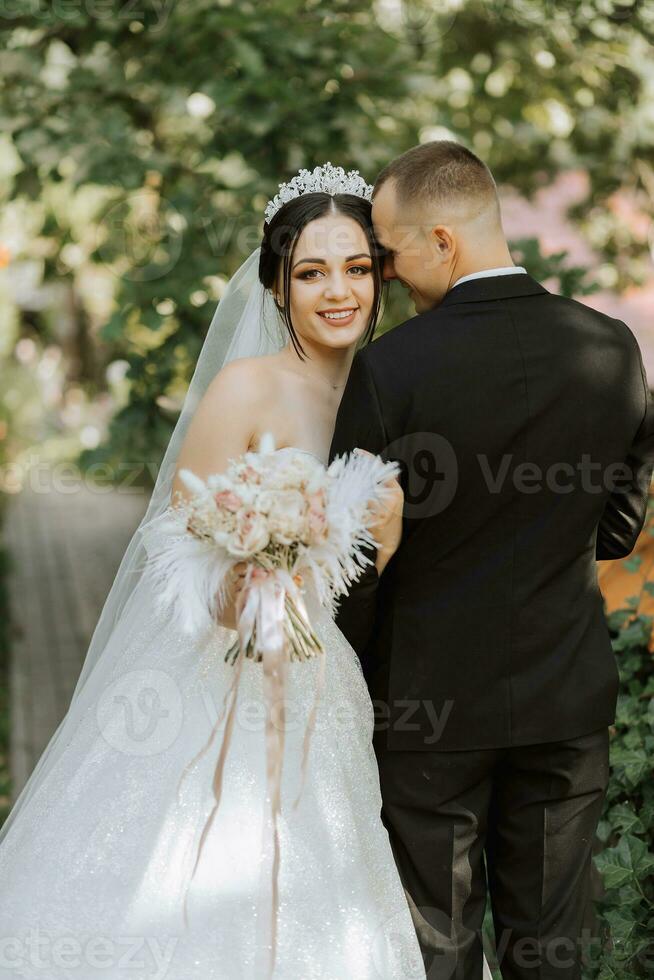 portrait of a young beautiful wedding couple in the garden, the bride in an off-the-shoulder wedding dress, the groom in a black classic suit photo