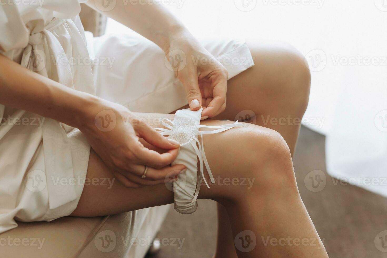 A young girl with a beautiful figure sits on a chair and puts on a garter. Wedding concept, the bride is preparing for the wedding photo