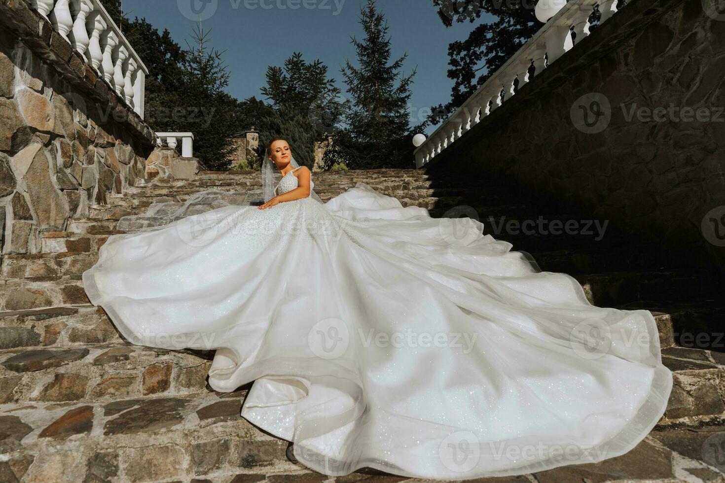 young beautiful bride in off-shoulder wedding dress lying on stone steps, fashion shot under harsh sunlight. The photo is taken from above