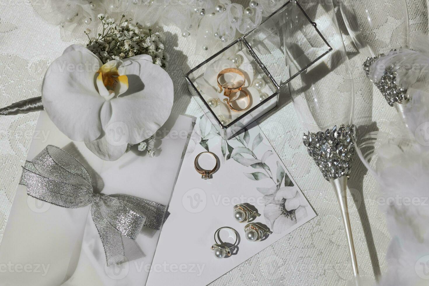 Boda detalles en plata color en un blanco antecedentes. Boda anillos y pendientes con perlas, lentes en plata soportes oro Boda anillos en un vaso caja. foto