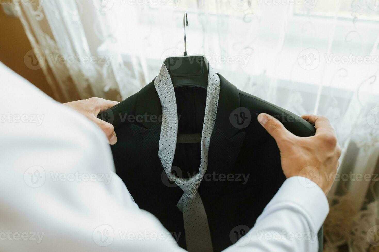Front view. A stylish watch. Men's style. Fashion. A business man in a white shirt is holding his black jacket against a window background. Business photo