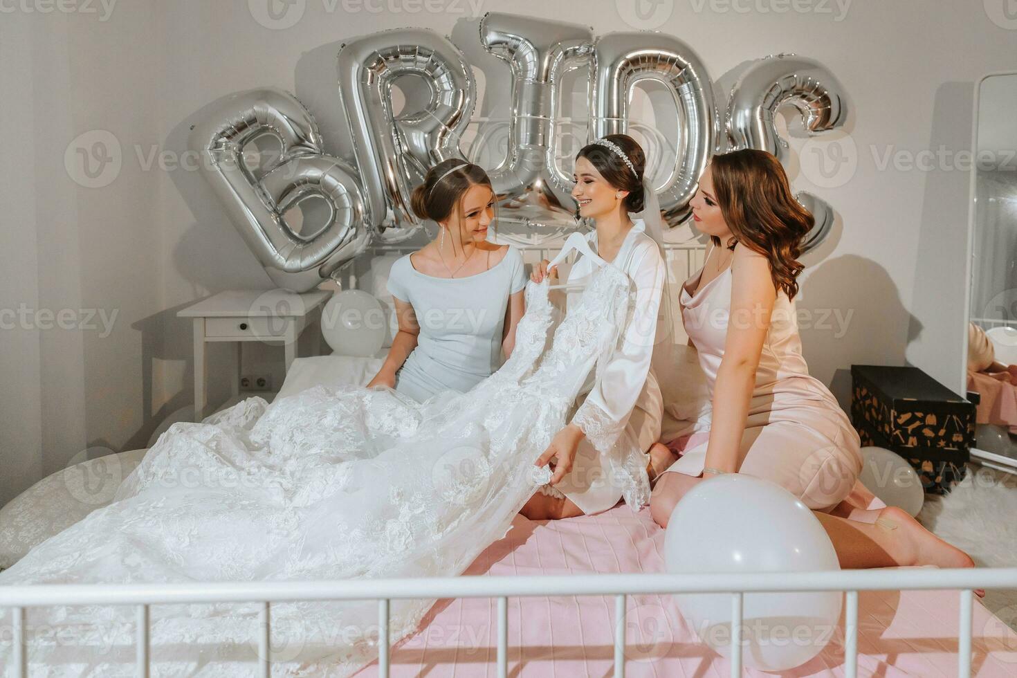 un hermosa joven novia y su novias son en pie en el cama y celebrando un despedida de soltera fiesta. final preparativos para el boda. el novia es esperando para el novio. mañana, novia. foto