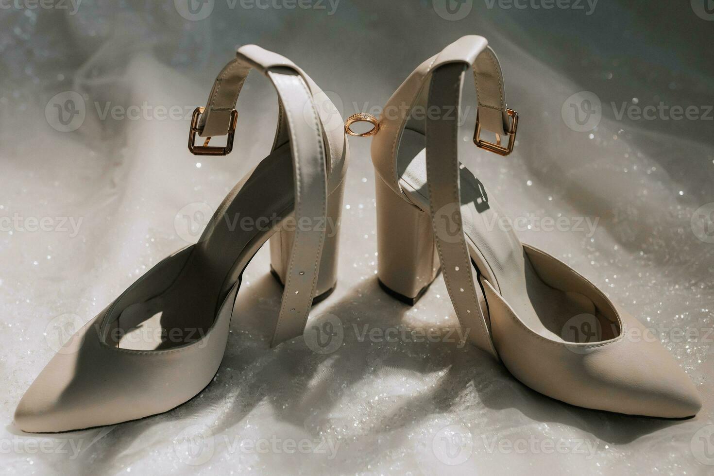 beige women's shoes are illuminated from above, next to it is a gold women's ring with a diamond. Up close photo