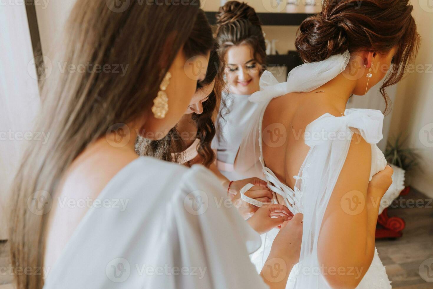 Portrait of the bride with her friends. The bride's friends fasten the bride's dress. Brunettes Open shoulders. photo