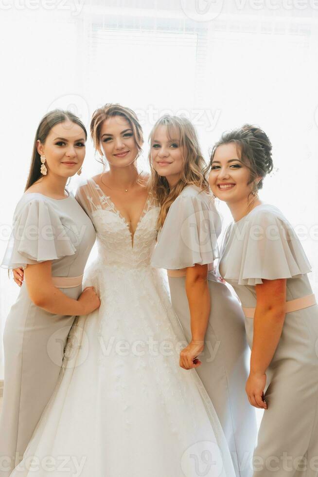 Portrait of the bride with her friends. The bride is posing in a voluminous white dress and her beautiful friends in gray evening dresses. Brunettes Open shoulders. Morning of the bride. photo