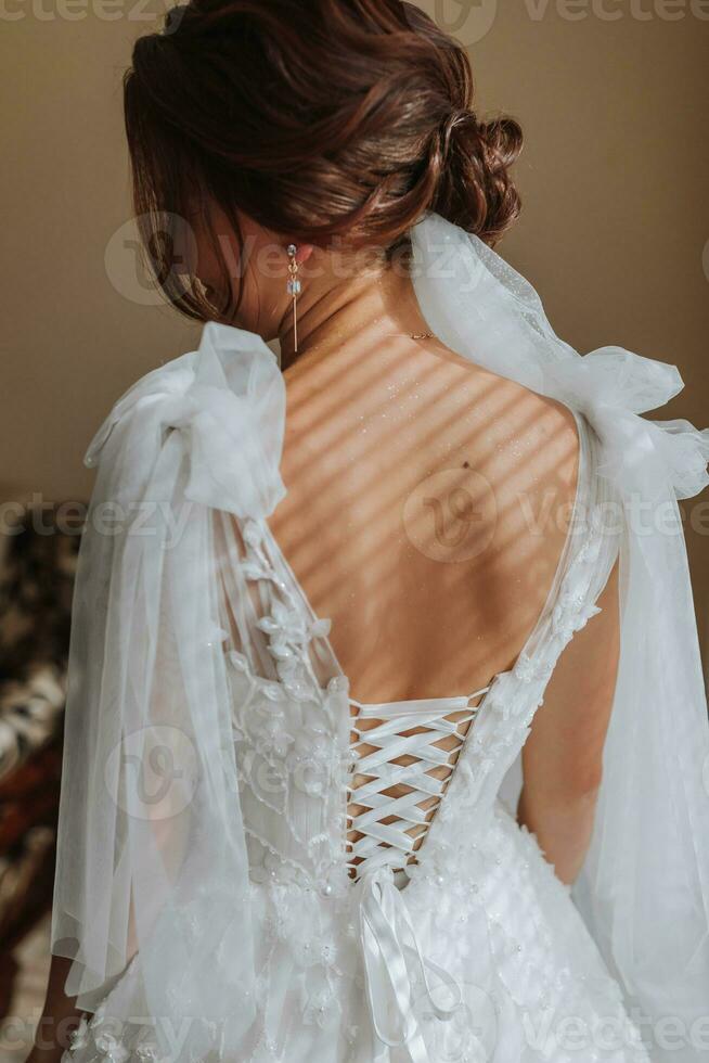 Photo of open beautiful shoulders of a bride wearing a wedding dress. Elegant hairstyle. Brown hair. Voluminous veil. Morning of the bride