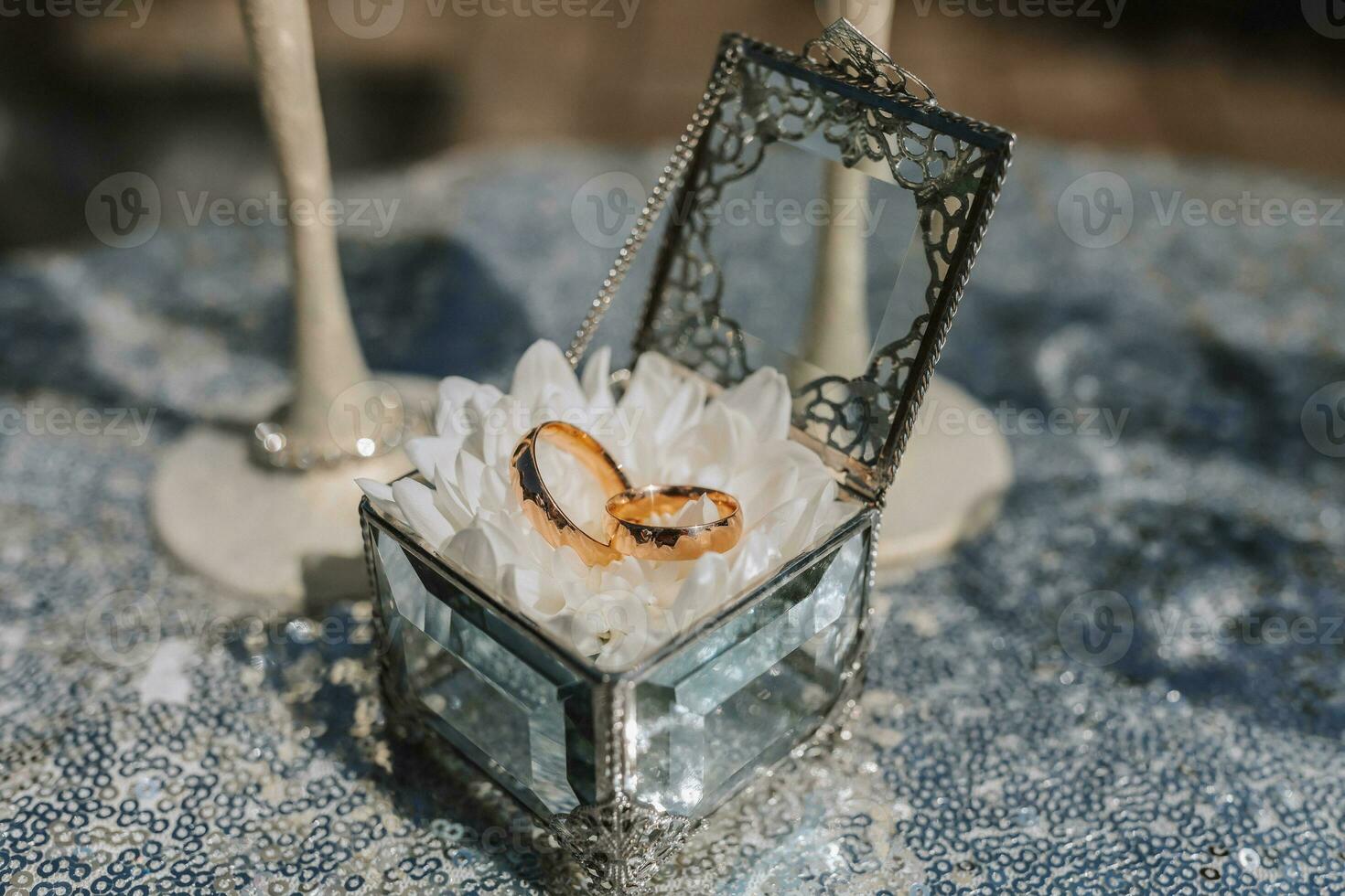 Wedding rings in a glass box, on a white flower. Wedding details. Holiday concept. The glasses are decorated with crystal flowers photo