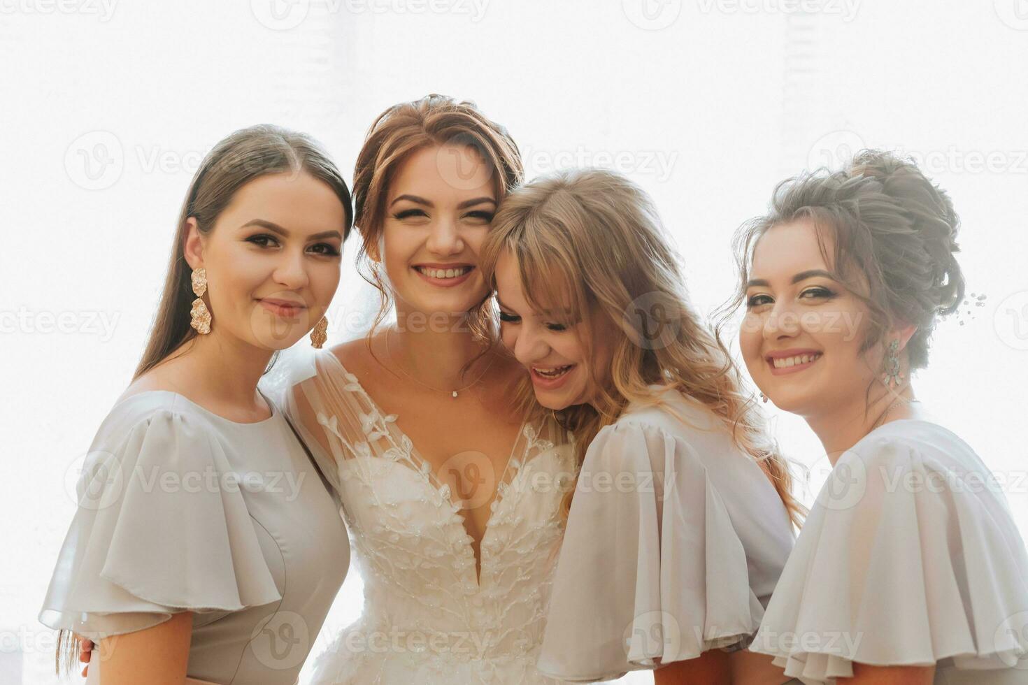 retrato de el novia con su amigos. el novia es posando en un voluminoso blanco vestir y su hermosa amigos en gris noche vestidos. morenas abierto espalda. Mañana de el novia. foto